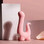 Aesthetic product shot of the HH Little Dino pleasure device with soft shadows on a minimalist pink background.