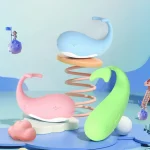 Lifestyle product display featuring the adorable whale-shaped clitoral stimulators in pastel blue, pink, and green colors on a playful, stylized background.