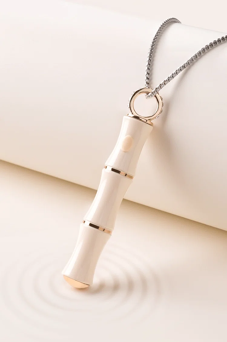 Aesthetic product photography of a bamboo-inspired necklace pendant vibrator creating soft ripples in water.