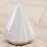 HH Crystal Kiss diamond-shaped clitoral stimulator with a white glitter finish on a soft fabric background.
