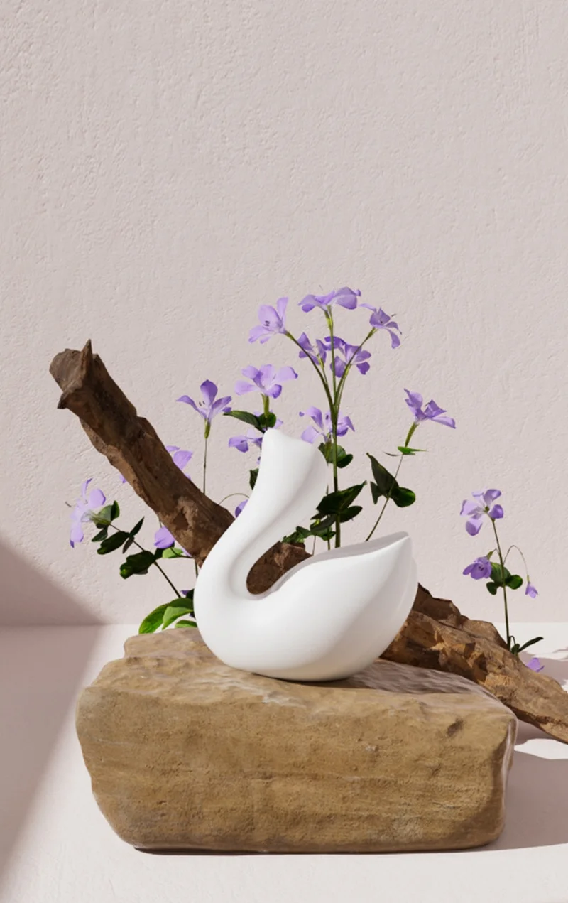 Minimalist lifestyle shot of the white Cygnus swan vibrator displayed as a piece of modern art with floral accents.