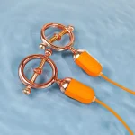 Rose gold metallic adjustable body clamps with waterproof orange silicone vibrating pods submerged in rippling blue water.
