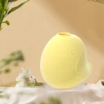 Pale yellow bird-shaped vibrator placed in a serene, nature-inspired setting with delicate white flowers, emphasizing its aesthetic appeal and discreet countertop presence.