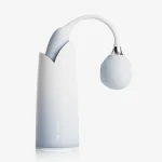 Dual-stimulation vibrator in a soft blue gradient standing in its custom home inspired charging and storage base.