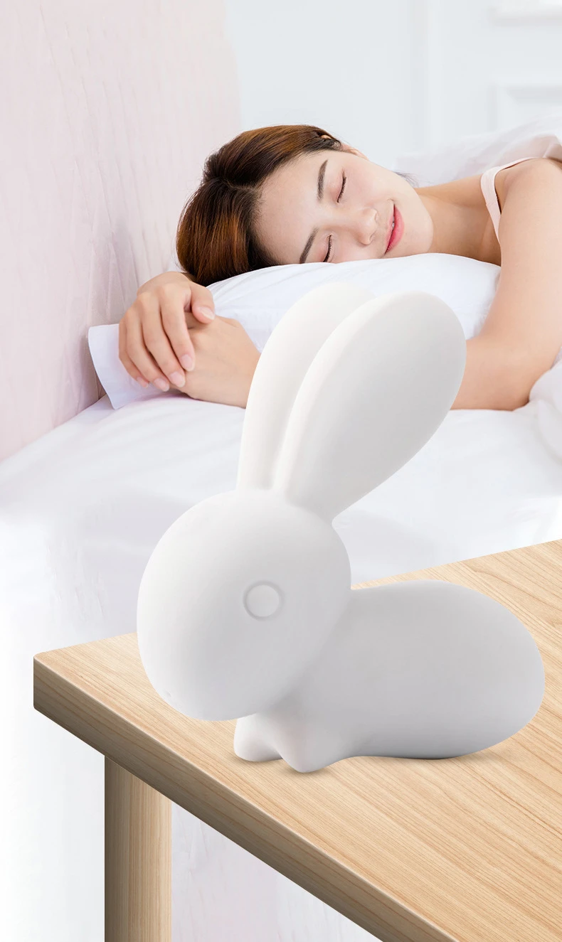Discreet bedside companion featuring a white bunny-shaped clitoral stimulator on a nightstand with a woman sleeping peacefully in the background.