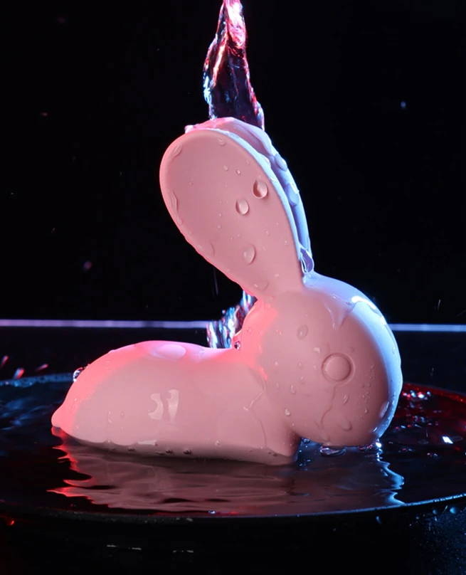 Waterproof rabbit stimulator under running water with blue and pink mood lighting to demonstrate its splash-proof capabilities for bath or shower use.