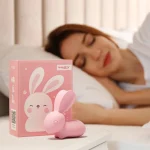 Lifestyle shot of the Happy Bunny pleasure tool sitting on a nightstand next to its retail gift box, emphasizing its quiet and discreet bedside presence.