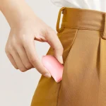 A person sliding a compact pink clitoral stimulator into a pants pocket, demonstrating the travel-friendly size and discreet portability of this handheld pleasure device.