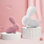 Two sleek rabbit-style personal massagers in soft pink and white displayed on minimalist pedestals, highlighting their modern aesthetic.