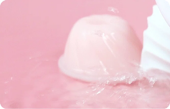 Close-up of a soft-touch pink silicone pleasure device being rinsed under water, demonstrating its fully waterproof and easy-to-clean design.