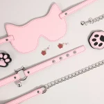 A complete pink kitty-themed intimacy set featuring a cat-ear blindfold, bell collar with leash, paw-print nipple clamps, and a decorative paw candle for sensory play.