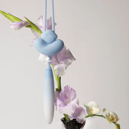 Aesthetic product photography of the Loom intimacy device suspended near floral orchids to highlight its artistic and discreet design.