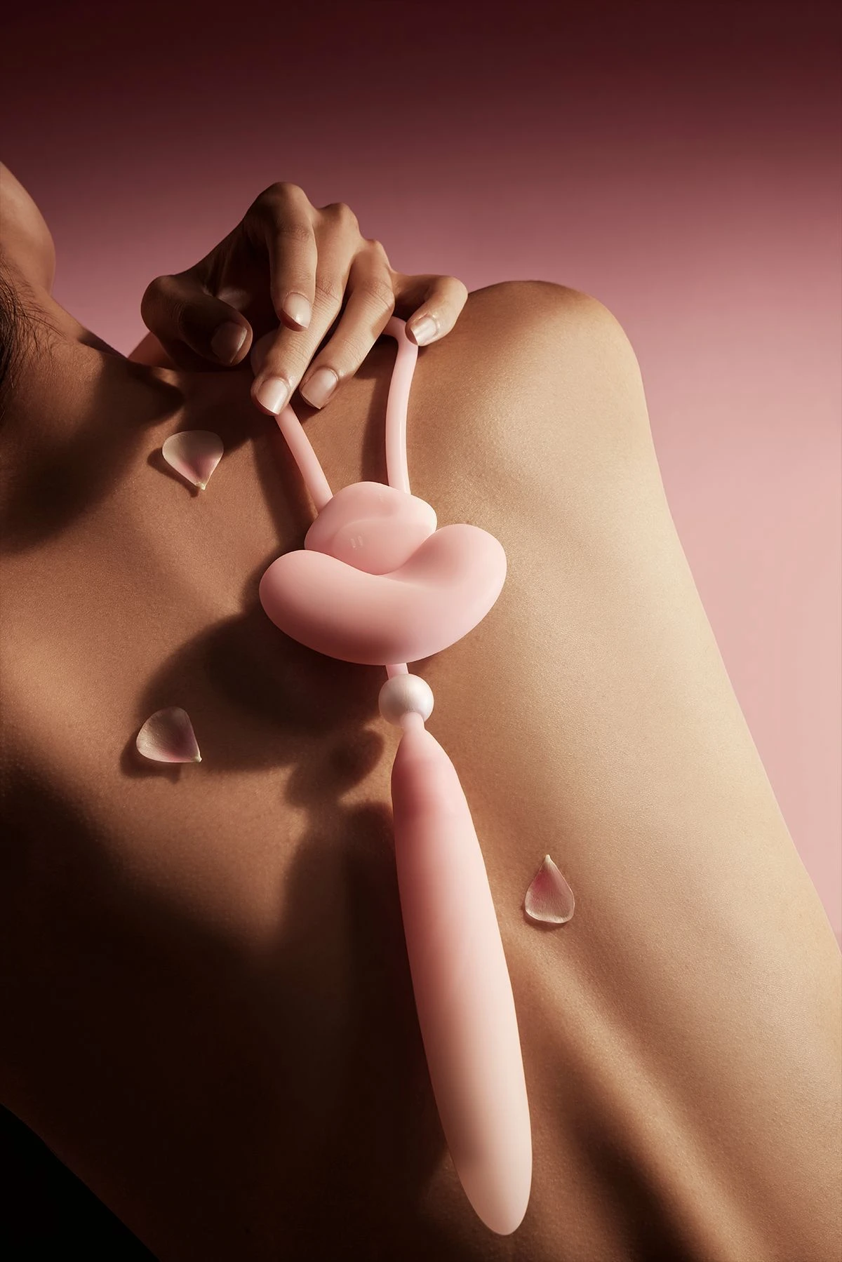 Lifestyle shot of a pink HH Loom wearable vibrator resting on a person’s back with decorative rose petals.