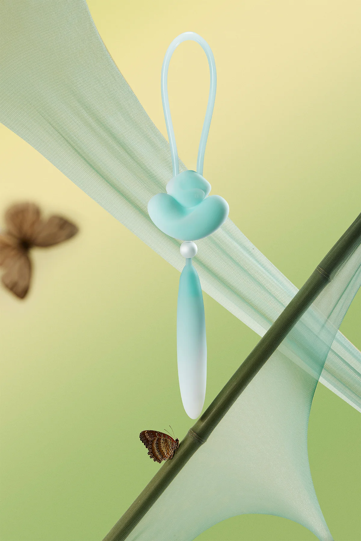 Mint green HH Loom intimacy tool suspended in a nature-inspired setting with silk fabric and butterflies for a soft, aesthetic appeal.