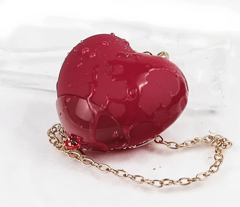 Red heart-shaped clitoral stimulator featuring a waterproof design with realistic water droplets and an elegant gold chain accessory.