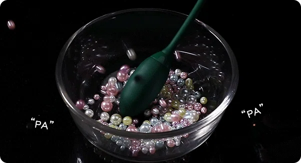 Action shot of the Luna Vault waterproof massage wand demonstrating powerful vibration intensity by displacing decorative pearls in a glass bowl.