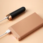 Black MILY pocket vibrator being charged via USB cable next to a power bank, demonstrating its travel-friendly and rechargeable design.