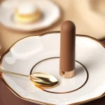 Creative product photography of a brown MILY clitoral vibrator placed on a luxury gold-rimmed ceramic plate to emphasize its sleek, "treat-yourself" appeal.