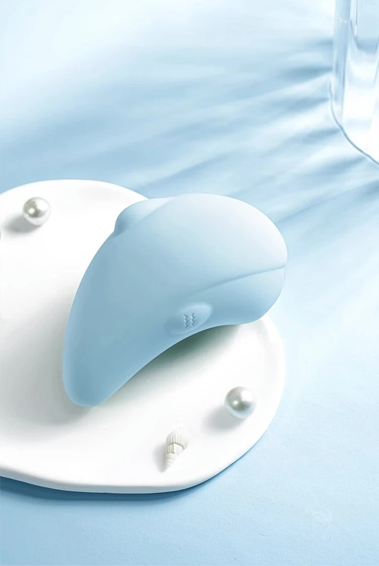 Dolphin-shaped clitoral stimulator in sky blue resting on a white aesthetic tray with pearls, highlighting its artistic and discreet design for bedside storage.