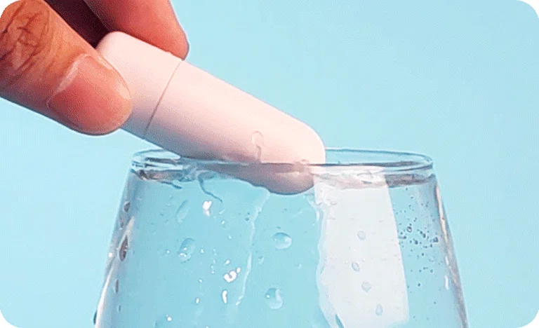 Waterproof pleasure device being submerged in a glass of water to showcase its seamless, splash-proof construction for easy cleaning.