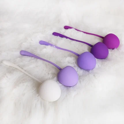 Lifestyle shot of five purple and white silicone kegel balls resting on a soft white faux-fur surface for a luxury aesthetic.