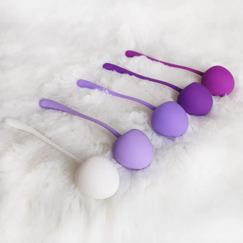 Lifestyle shot of five purple and white silicone kegel balls resting on a soft white faux-fur surface for a luxury aesthetic.