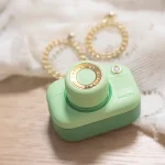 Aesthetic lifestyle shot of the Snapshot camera-inspired clitoral suction device in mint green resting on a bedside table with jewelry.