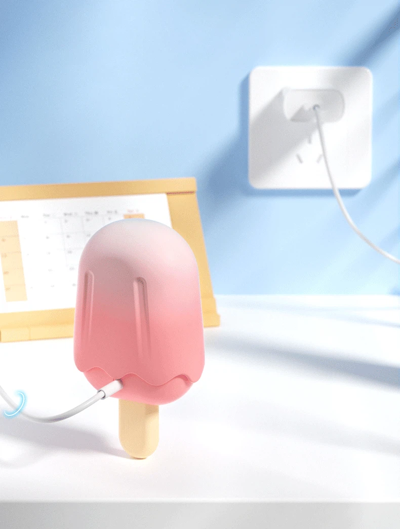 Rechargeable popsicle vibrator plugged into a USB wall charger on a white nightstand for convenient bedside power.
