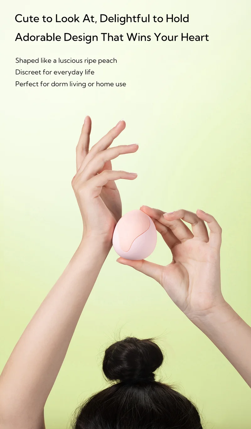 Hands holding peach-shaped personal massager against soft pastel background