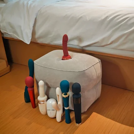 Cube stool displayed beside a bed with multiple adult toys arranged around it