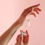 Hand holding clear glass anal plug against pink background Discreet Sex Toys Brand - HooHss