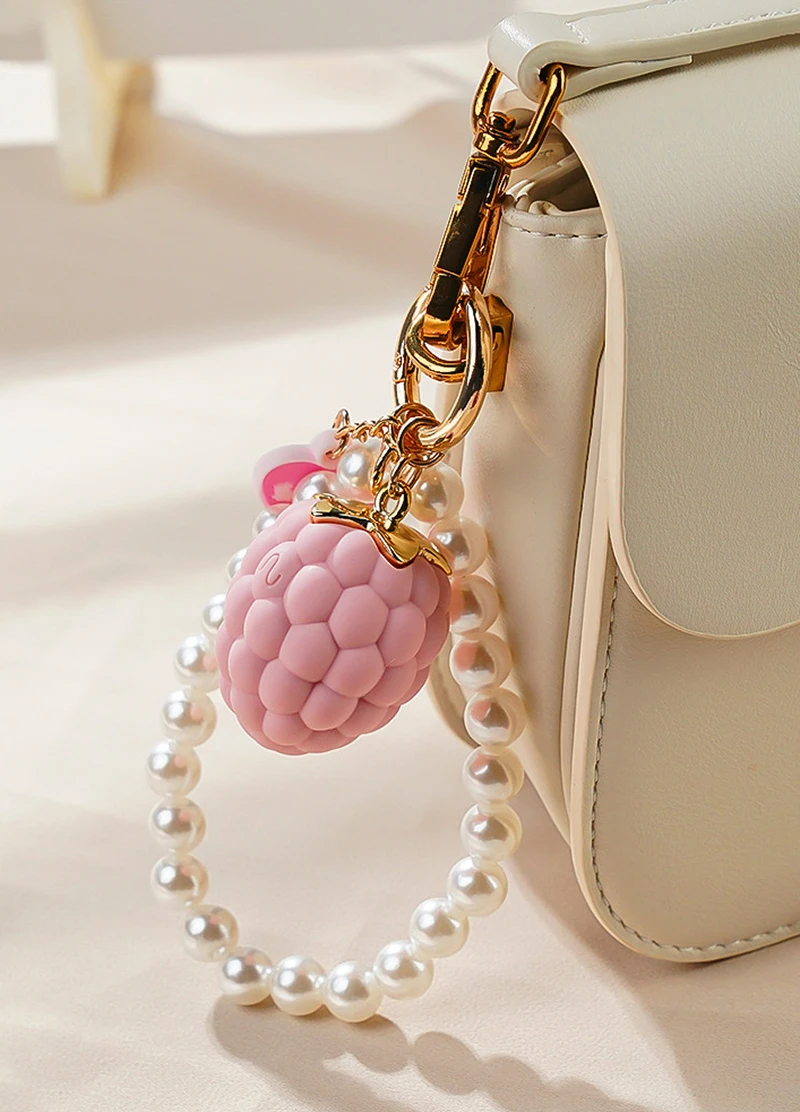 Pink berry-shaped vibrating bracelet charm clipped to a white handbag with pearl loop Discreet Sex Toys Brand - HooHss